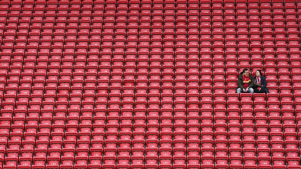 People sit surrounded by empty seats as they wait for the start of the English Premier League soccer match between Liverpool and Bournemouth at Anfield stadium in Liverpool, England, Saturday, March 7, 2020. (AP Photo/Jon Super)