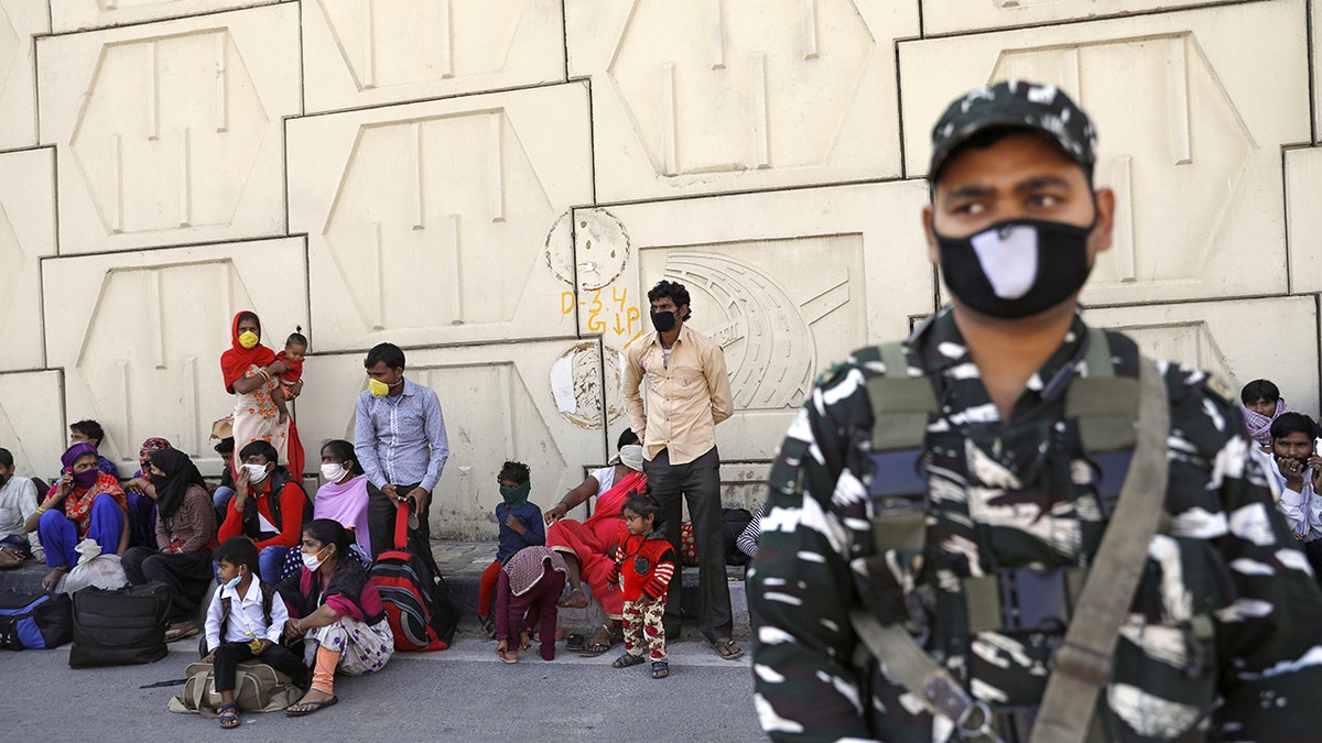 A soldier on guard stands next to migrant workers as they wait for buses along a highway with their families to return to their villages. (REUTERS/Anushree Fadnavis)