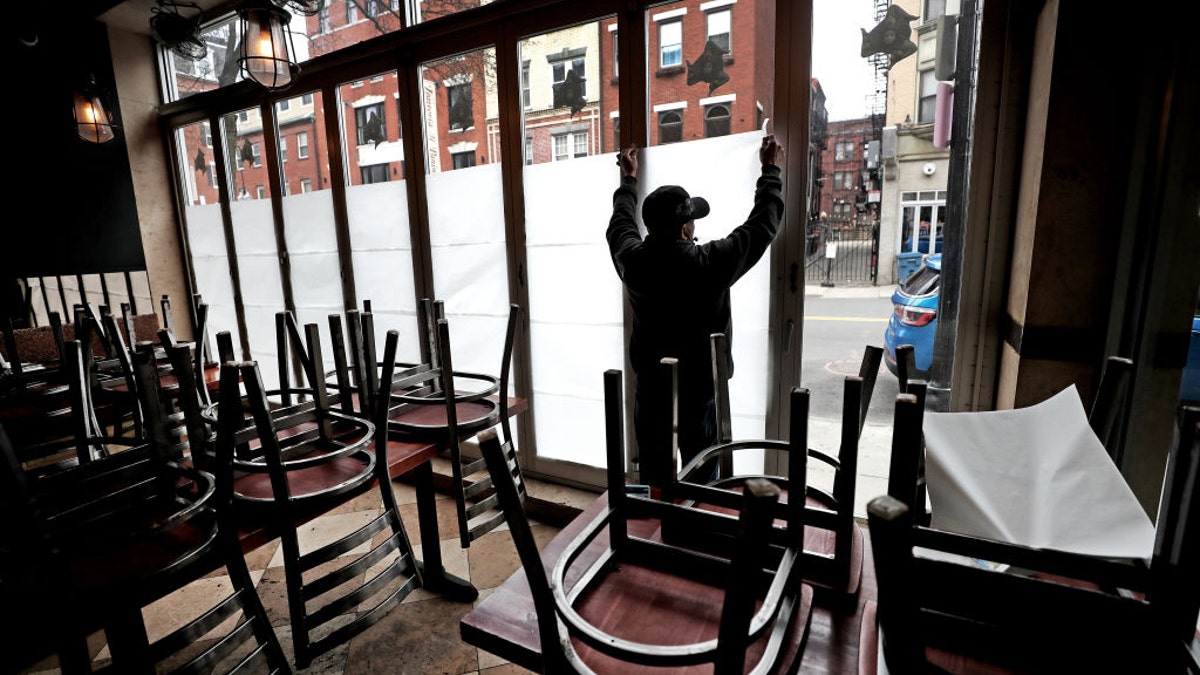 An employee at a restaurant in Boston tapes the eatery's windows after temporarily closing to customers on March 25.