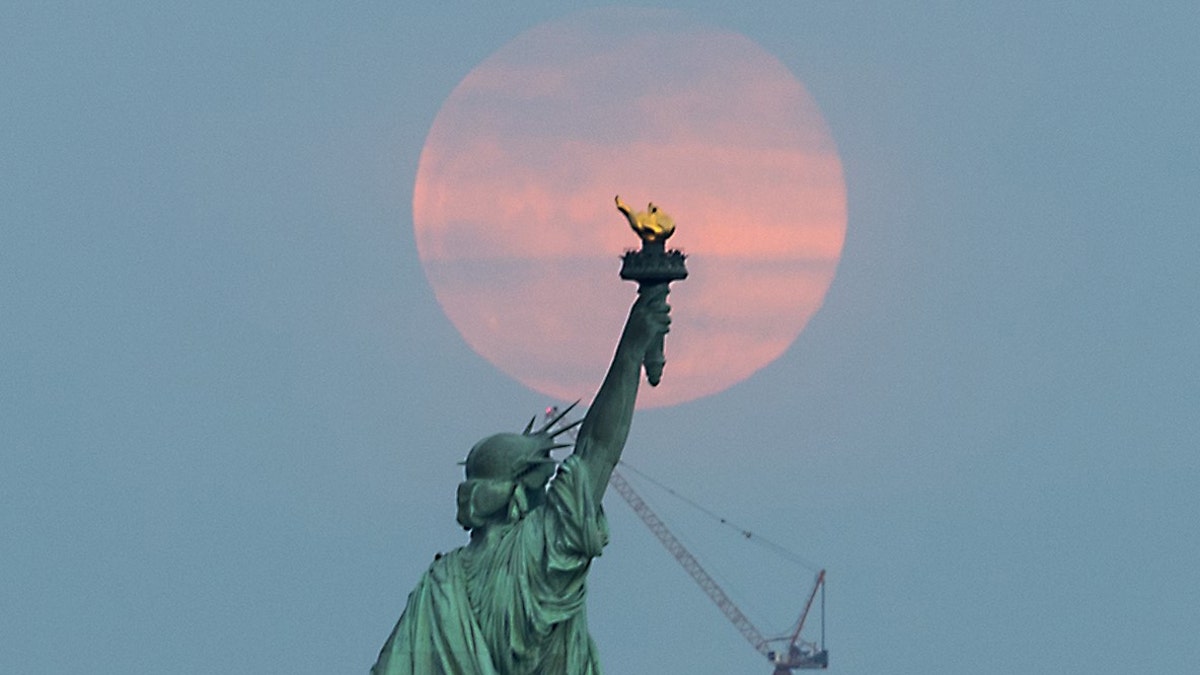 The 'Super Worm Equinox Moon' rises behind the Statue of Liberty in New York, on March 20, 2019.