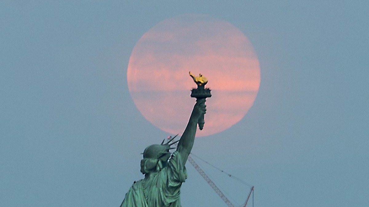 The 'Super Worm Equinox Moon' rises behind the Statue of Liberty in New York, on March 20, 2019.
