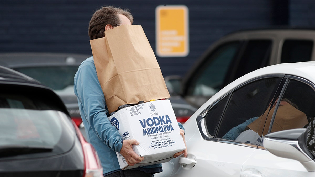 A shopper struggles to open the back door of his sedan while juggling his purchase from a liquor store