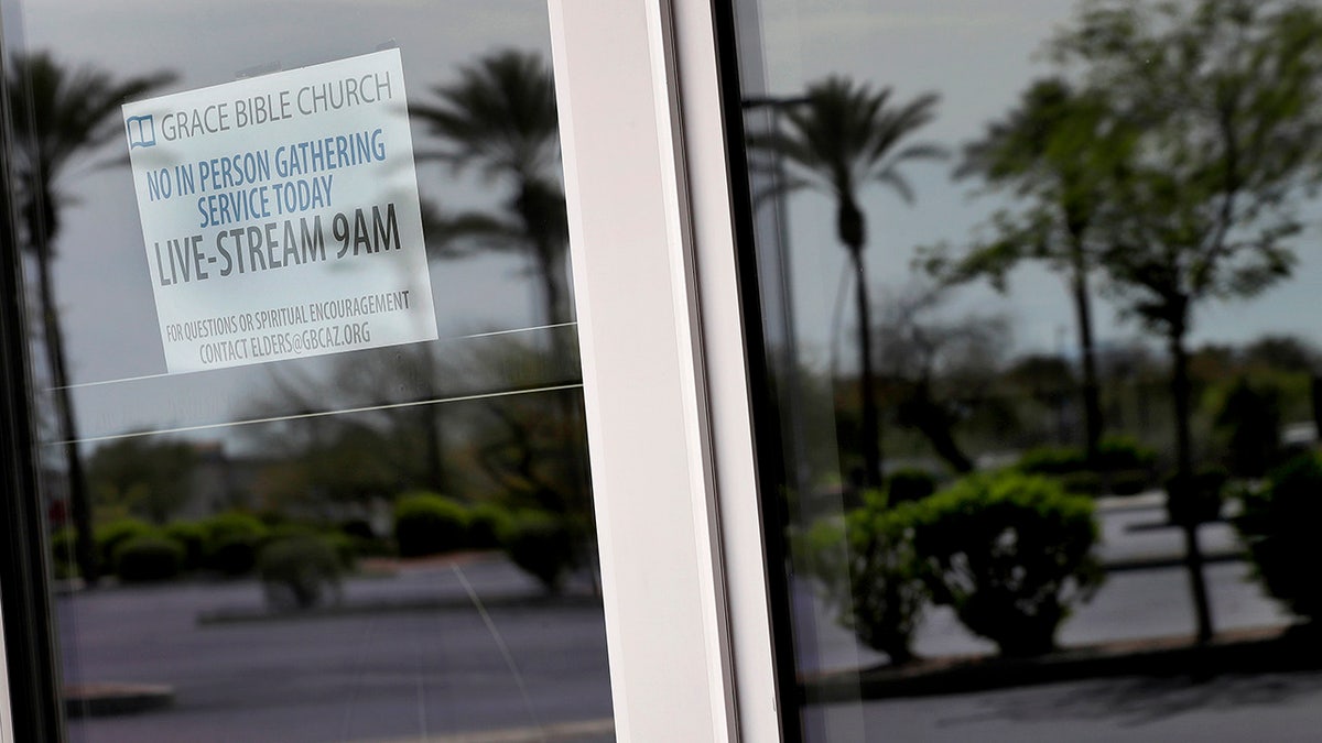 An empty parking lot is reflected in the doors of Grace Bible Church Sunday, March 22, 2020, in Tempe, Ariz. Many houses of worship have suspended all in-person services and programs and moved to online services in compliance with CDC guidelines to promote social distancing in the effort to slow the spread of the COVID-19 coronavirus. (AP Photo/Matt York)