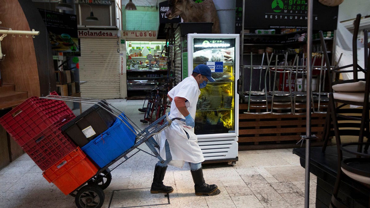 An employee wearing a protective face mask and disposable gloves, hauls crates with the aid of a trolley through the popular and normally crowded San Juan food market, in Mexico City, Wednesday, March 25, 2020.  (AP Photo/Fernando Llano)