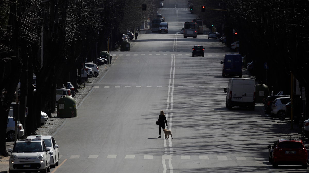 A woman walks her dog in the EUR neighborhood in Rome, Monday, March 23, 2020.