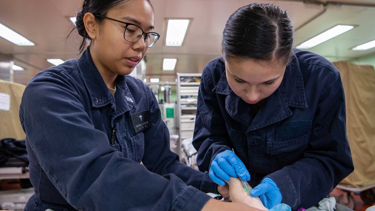 Larraine Castimo, from Orosi, Calif., and Alexandria Loyola, from Castlerock, Colo., practice administering an IV needle during a venipuncture training aboard USNS on Wednesday. Mercy deployed in support of the nation's COVID-19 response effort.