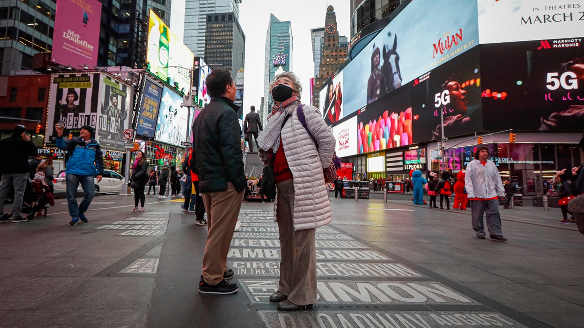 A pedestrian wearing a face mask stops in Times Square, Thursday, March 12, 2020, in New York. New York City Mayor Bill de Blasio said Thursday he will announce new restrictions on gatherings to halt the spread of the new coronavirus in the coming days. For most people, the new coronavirus causes only mild or moderate symptoms. For some it can cause more severe illness. (AP Photo/John Minchillo)