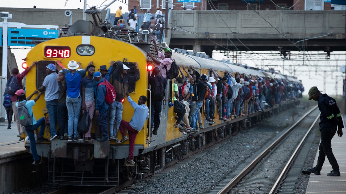 Train commuters hold on to the side of an overcrowded passenger train in Soweto, South Africa, Monday, March 16, 2020.