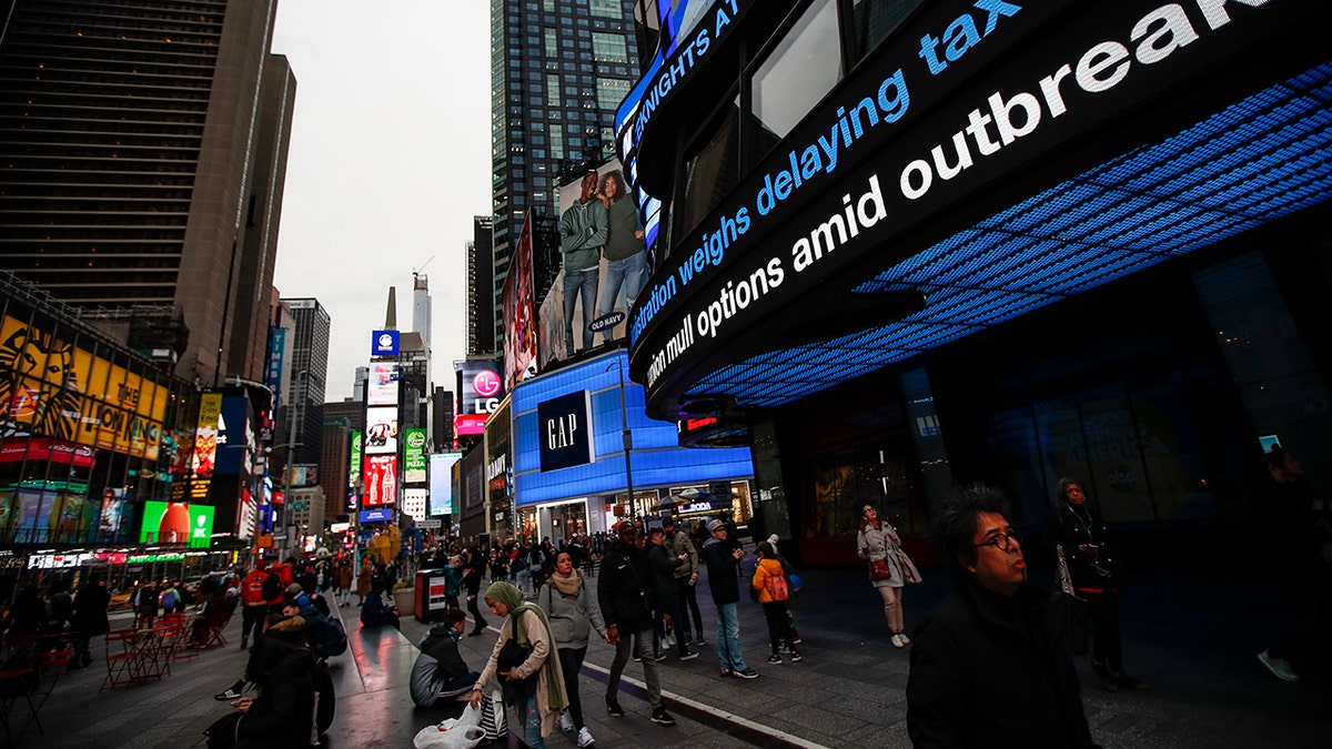 Pedestrians pass under a news ticker in Times Square, Wednesday, March 11, 2020, in New York, N.Y. The number of coronavirus cases in New York state jumped Sunday to more than 100, a spread that forced the suspension of classes at schools across the state, including a district that has a faculty member with a positive test and Columbia and Hofstra universities. For most people, the new coronavirus causes only mild or moderate symptoms. For some it can cause more severe illness. 