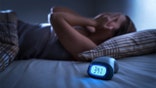 Sleepless woman suffering from insomnia, sleep apnea or stress. Tired and exhausted lady. Headache or migraine. Awake in the middle of the night. Frustrated person with problem. Alarm clock with time.