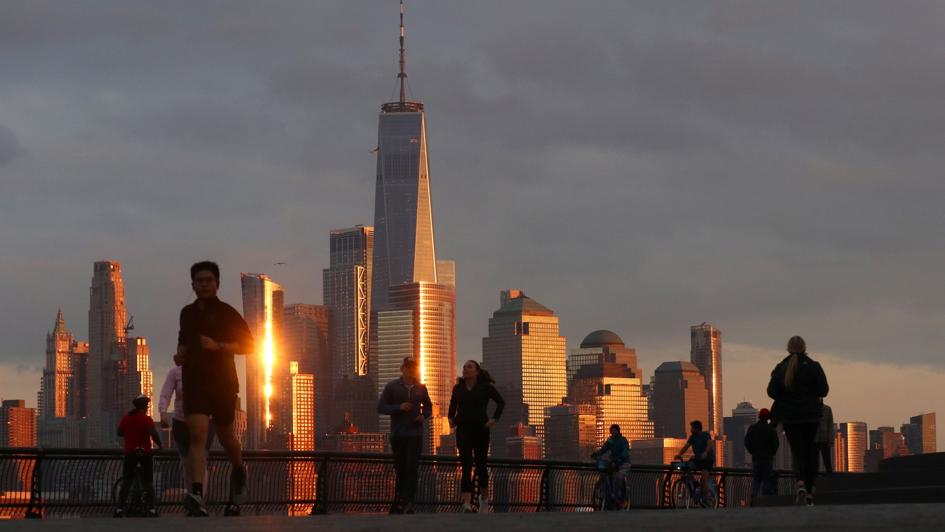 People walk and jog in front of the skyline of lower Manhattan in New York City as the sun sets in Hoboken, N.J., March 17, 2020.