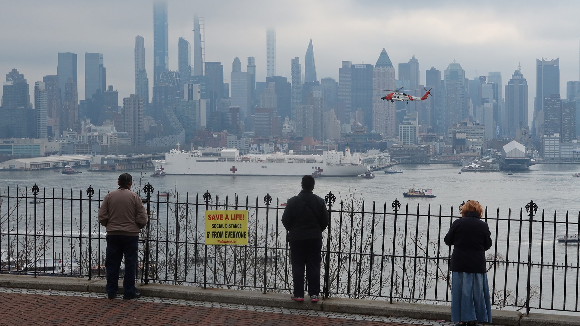 People social distance as they watch the USNS Comfort arrive in port on the Hudson River in New York City, March 30, 2020.