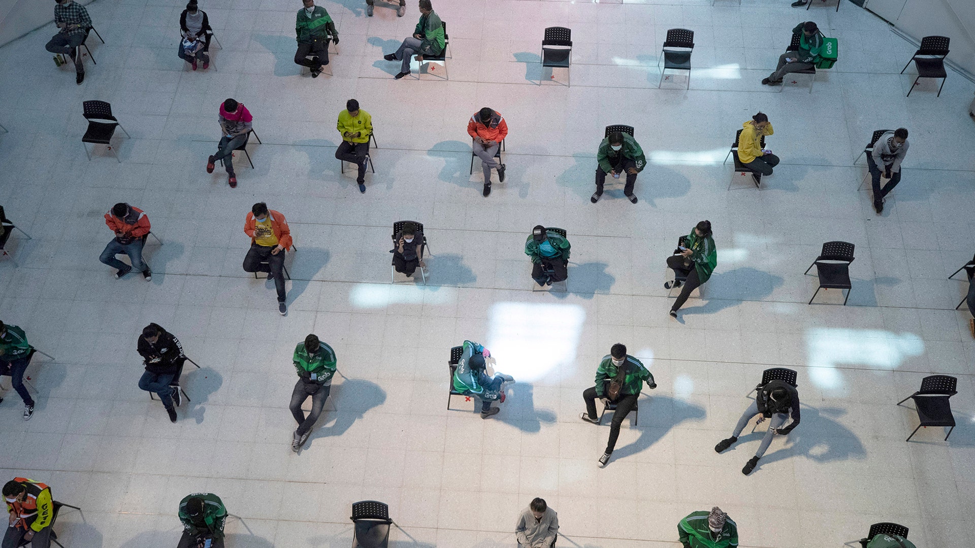 People practice social distancing as they sit on chairs spread apart in a waiting area for take-away food orders at a shopping mall in Bangkok, March 24, 2020. 