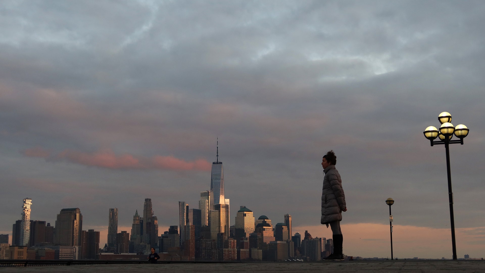 A woman stands in front of the skyline of lower Manhattin on Pier A in Hoboken, N.J., March 17, 2020.