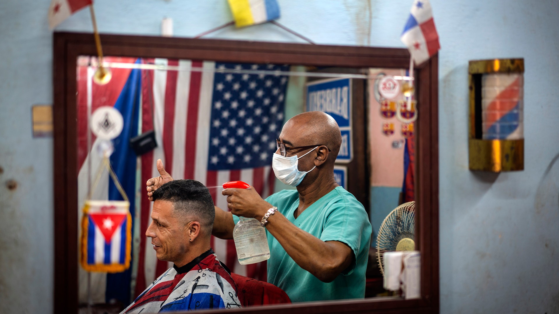 Barber Eugenio Lafargue wearing a protective face mask as a precaution against the spread of the coronavirus is reflected in a mirror as he styles a customer's hair, in Havana, Cuba, March 25, 2020. 