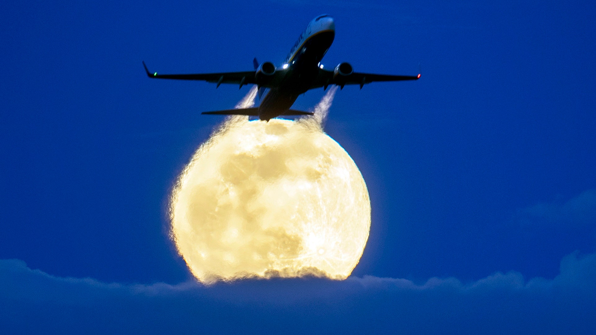 An aircraft passes the rising Super Worm Moon as it breaks through clouds in Frankfurt, Germany, March 9, 2020. 