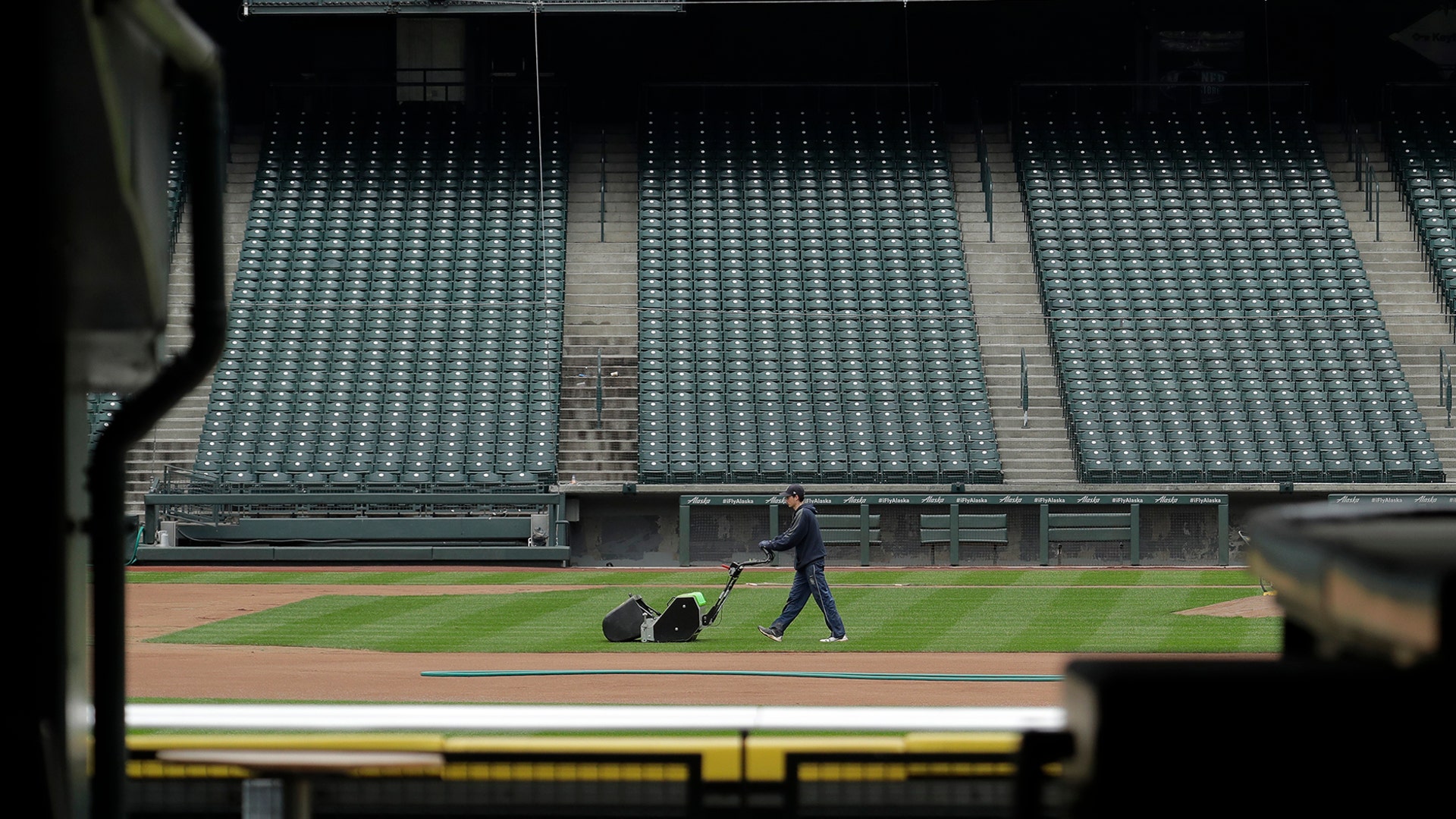 A grounds crew worker cuts the infield grass in front of empty seats around the time when the first pitch would have been thrown in the Mariners' Opening Day baseball game in Seattle, March 26, 2020. 