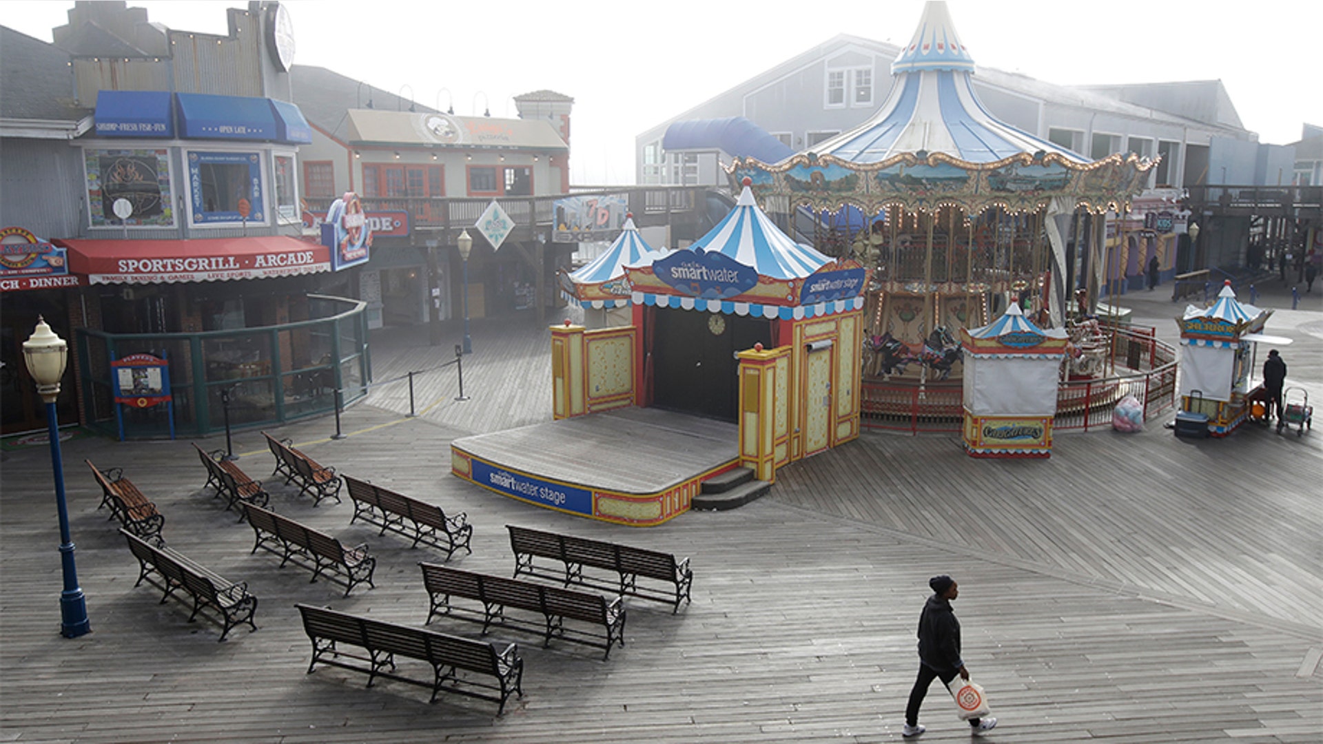 San Francisco, California: A woman walking in front of a stage and carousel at an empty Pier 39, Thursday, March 12, 2020.