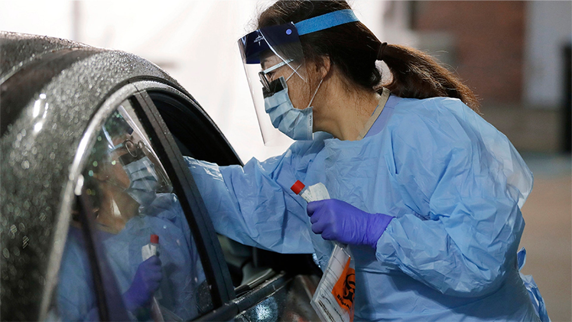 A nurse at a drive-up coronavirus testing station set up by the University of Washington Medical Center uses a swab to take a sample from the nose of a person in a car in Seattle, Wash., March 13, 2020.