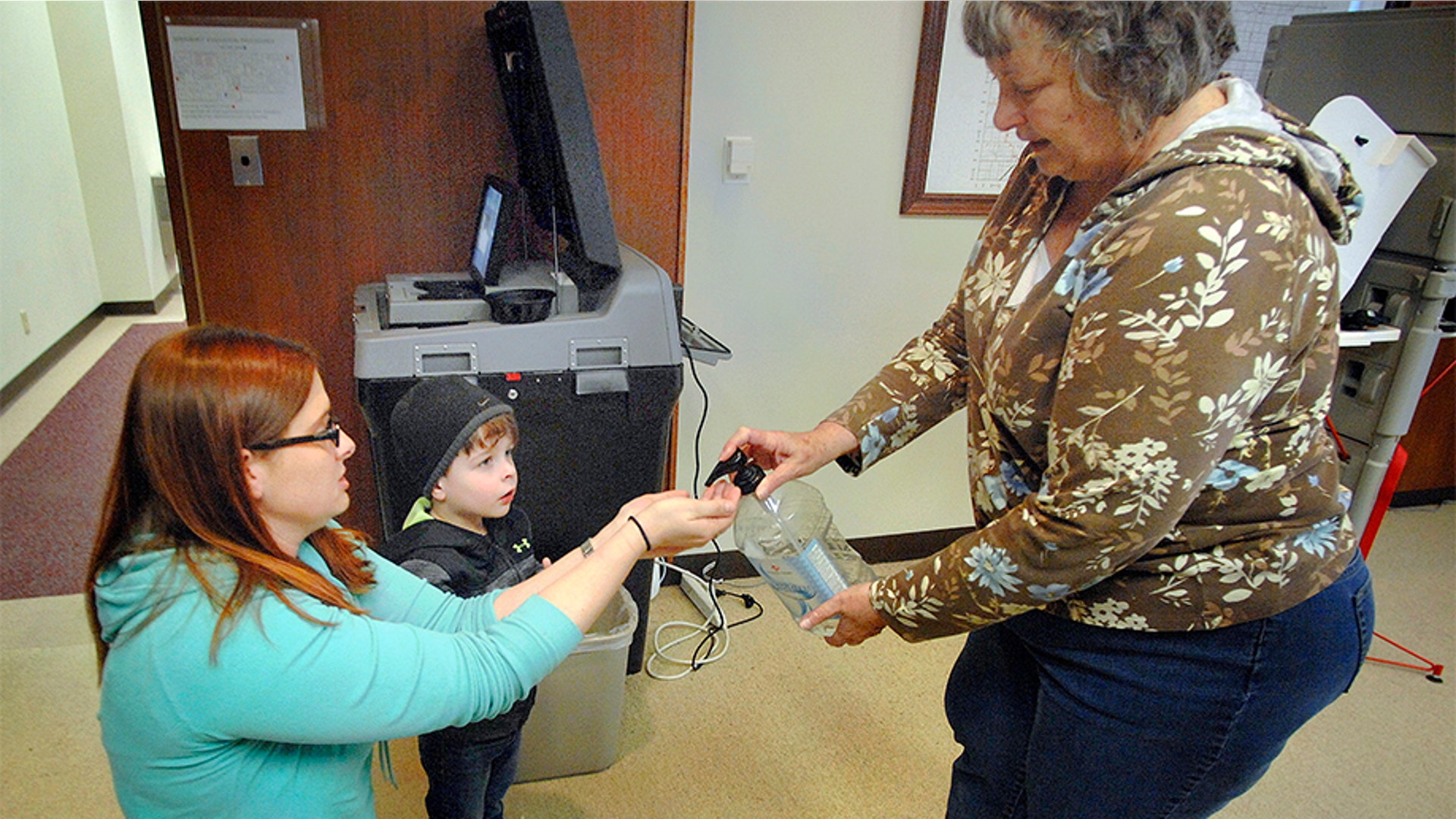 Bloomington Election Commission Judge Kim Osterbrock, right, squeezing hand sanitizer for voter Angela Kuppersmith and her son, Wyatt, 3, after they cast her early vote, at the Government Center in Bloomington. 