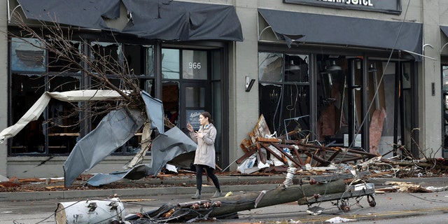 A woman walks past buildings damaged by storms Tuesday, March 3, 2020, in Nashville, Tenn.