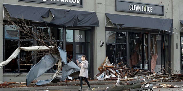 A woman walks past buildings damaged by storms Tuesday, March 3, 2020, in Nashville, Tenn.