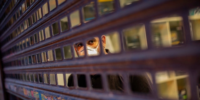 A man, wearing a face mask due the coronavirus outbreak, looks from behind a gate in downtown Madrid, Spain, Tuesday, March 24, 2020. More than 1.5 billion around the world have been told to stay in their homes. For most people, the new coronavirus causes only mild or moderate symptoms. For some it can cause a more serious illness. (AP Photo/Bernat Armangue)