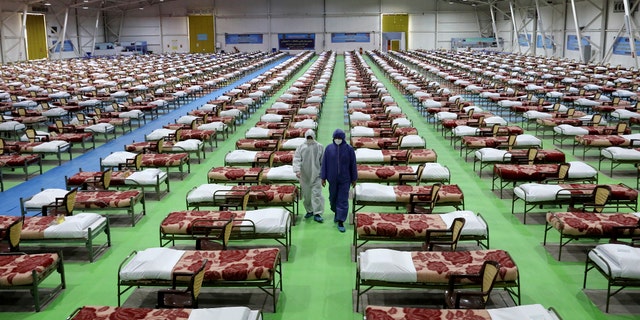 People in protective clothing walk past rows of beds at a temporary 2,000-bed hospital for COVID-19 coronavirus patients set up by the Iranian army at the international exhibition center in northern Tehran, Iran, on Thursday, March 26, 2020. (AP Photo/Ebrahim Noroozi)