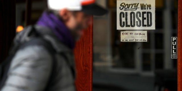 A pedestrian walks by a closed sign on the door of a restaurant on March 17 in San Francisco.