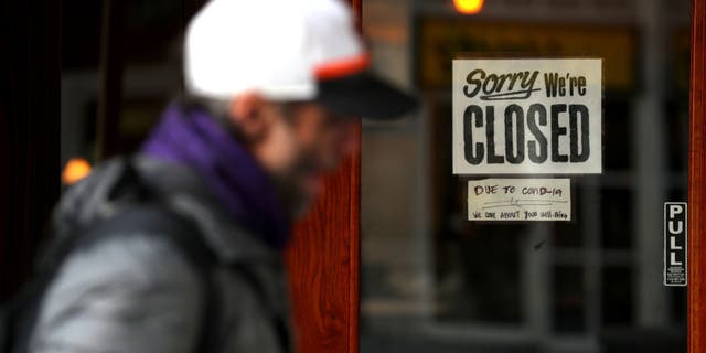 A pedestrian walks by a closed sign on the door of a restaurant on March 17 in San Francisco.