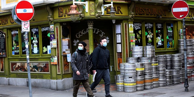 Tourists wearing face masks walk past a closed pub in Dublin city center on March 16 (AP Photo / Peter Morrison, File)