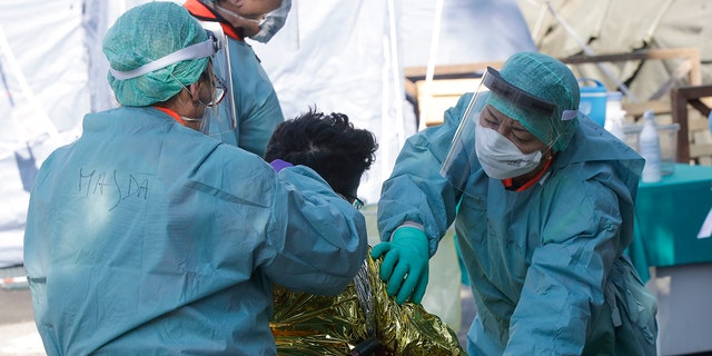 A man wrapped in a survival blanket is assisted by medical staff upon his arrival at one of the emergency structures that were set up to ease procedures at the Brescia hospital, Italy, Monday, March 16, 2020.