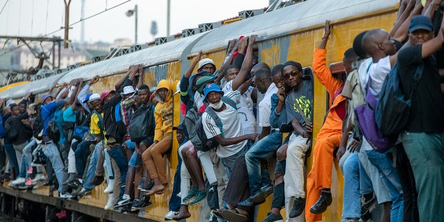 Train commuters hold on to the side of an overcrowded passenger train in Soweto, South Africa, Monday, March 16, 2020. South Africa will revoke nearly 10,000 visas issued this year to people from China and Iran, and visas will now be required for other high-risk countries that had been visa-free, including Italy and the United States. (AP Photo/Themba Hadebe)