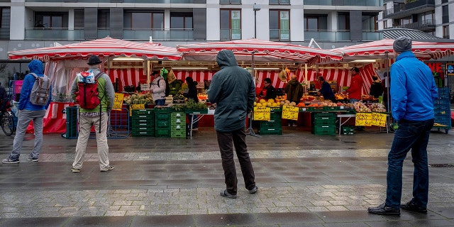 People keep distance as they queue on a small weekly market in Frankfurt, Germany, early Saturday, March 21, 2020.