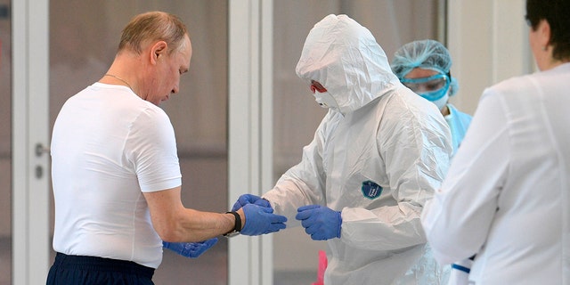 Russian President Vladimir Putin, left, dons gloves during his visit to the hospital for coronavirus patients in Kommunarka settlement, outside Moscow, Russia, Tuesday, March 24, 2020.