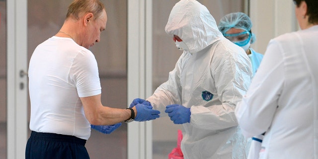 Russian President Vladimir Putin, left, dons gloves during his visit to the hospital for coronavirus patients in Kommunarka settlement, outside Moscow, Russia, Tuesday, March 24, 2020.