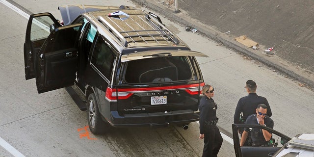 Los Angeles police officers stand after a pursuit of a stolen hearse with a casket and body inside on Interstate 110 in South Los Angeles last week. The hearse was stolen from outside a Greek Orthodox church in East Pasadena on Wednesday night. (AP Photo/Reed Saxon)