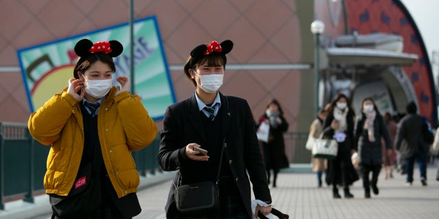 Two visitors with masks and Minnie Mouse ear headbands leave Tokyo Disneyland in Urayasu, near Tokyo, Friday, Feb. 28.