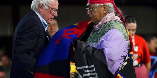 FILE - In this Sept. 22, 2019, file photo, Democratic presidential candidate U.S. Sen. Bernie Sanders receives an honor blanket from Cornel Pewewardy at the annual Comanche Nation Fair Powwow, in Lawton, Okla. Sanders hopes Super Tuesday, March, 3, 2020, in Oklahoma will be a repeat of his performance four years ago, while the rest of the Democratic field hope to get a foothold in the Sooner State as voters in 14 states head to the polls.(AP Photo/Gerardo Bello, File)