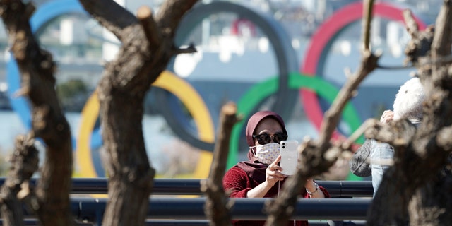 A tourist wearing a protective mask takes a photo with the Olympic rings in the background Tuesday, March 3, 2020, at Tokyo's Odaiba district. The spreading virus from China has put the Tokyo Olympics at risk. The Olympics are to open on July 24 - less than five months away. (AP Photo/Eugene Hoshiko)