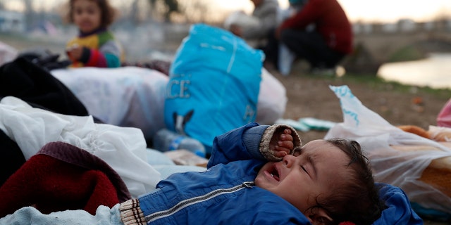 A baby cries as migrants gather next to a river in Edirne, Turkey, near Turkish-Greek border on Wednesday, March 4, 2020. Facing a potential wave of nearly a million people fleeing fighting in northern Syria, Turkey has thrown open its borders with Greece to thousands of refugees and other migrants trying to enter Europe, and has threatened to send "millions" more. (AP Photo/Darko Bandic)