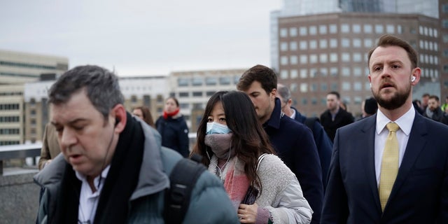 A woman wearing a face mask walks across London Bridge in London. British authorities laid out plans Tuesday to confront a COVID-19 epidemic, saying that the new coronavirus could spread within weeks from a few dozen confirmed cases to millions of infections, with thousands of people in the U.K. at risk of death.