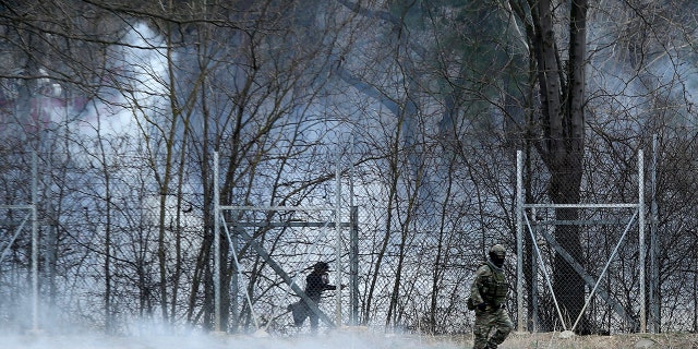 A Greek army officer patrols as a migrant is seen at the Turkish side at the Greek-Turkish border in Kastanies on Wednesday, March 4, 2020. Facing a potential wave of nearly a million people fleeing fighting in northern Syria, Turkey has thrown open its borders with Greece to thousands of refugees and other migrants trying to enter Europe, and has threatened to send "millions" more. (AP Photo/Giannis Papanikos)