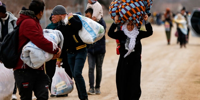 A woman carries her belongings as she walks with other migrants at the Turkish-Greek border in Pazarkule on Wednesday, March 4, 2020. Greek authorities fired tear gas and stun grenades Wednesday morning to repulse a push by migrants to cross its land border from Turkey, as pressure continued along its frontier after Turkey said its own border with Europe was open to whoever wanted to cross. (AP Photo/Emrah Gurel)