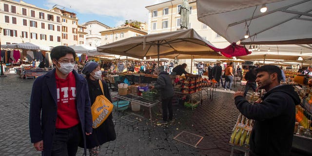 A seller calls for customers as a couple wearing face masks walks by, at the Campo de' Fiori street market, in Rome, on March 7.