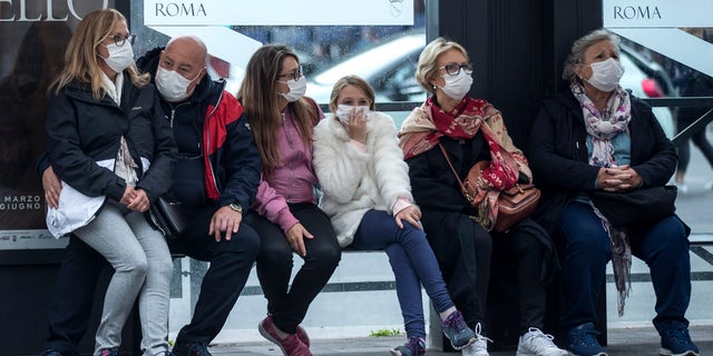 People wait at a bus stop, in Rome, Monday, March 9, 2020. Italy announced a sweeping quarantine early Sunday for its northern regions, igniting travel chaos as it restricted the movements of a quarter of its population in a bid to halt the new coronavirus' relentless march across Europe. (Roberto Monaldo/LaPresse via AP)
