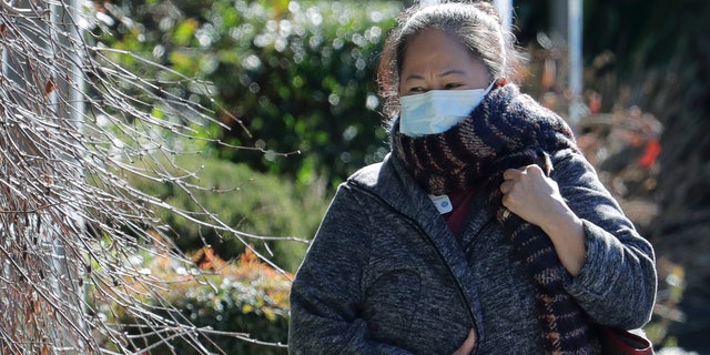 A worker at the Life Care Center in Kirkland, Wash., wears a mask and a scarf as she walks away from the facility, Monday, March 9, 2020, near Seattle. (AP Photo/Ted S. Warren)