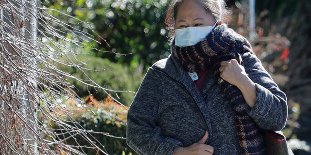 A worker at the Life Care Center in Kirkland, Wash., wears a mask and a scarf as she walks away from the facility, Monday, March 9, 2020, near Seattle. (AP Photo/Ted S. Warren)