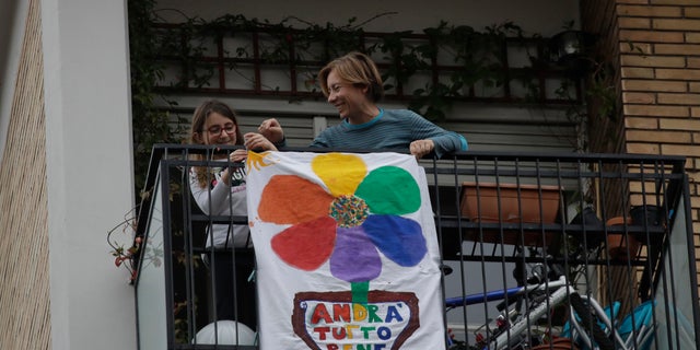 In this March 13 photo, 8-year hold Flavia is flanked by her mother Silvia as they place a banner reading "Everything will be alright" on the balcony of their apartment in Rome, Italy. (AP Photo/Alessandra Tarantino)