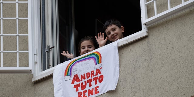 In this March 13 photo, Francesco and Greta Innominati wave after placing a banner reading "Everything is gone be all right" out of a window of their apartment in Rome, Italy. (AP Photo/Alessandra Tarantino)